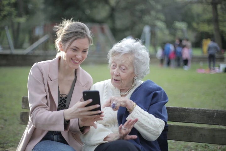 elderly woman sitting on park bench with daughter looking at mobile phone